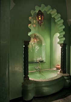 a bathroom with green walls and an arched window above the bathtub is lit by a chandelier