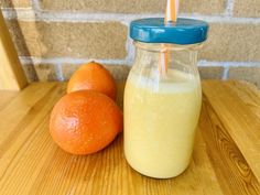 two oranges sitting next to a glass with a straw in it on a wooden table