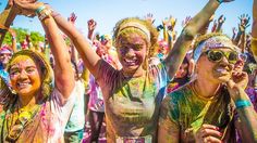 two women covered in colored paint are holding their hands up to the sky and smiling