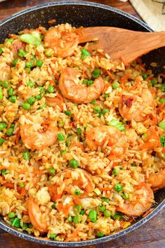 a skillet filled with shrimp and rice on top of a wooden table