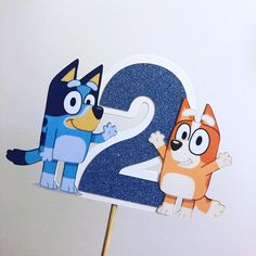 a cake topper with the number two on it and cartoon characters in blue, orange and white