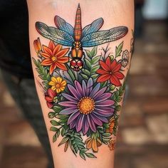 a woman's leg with flowers and dragonfly tattoo on her thigh, which is painted in bright colors