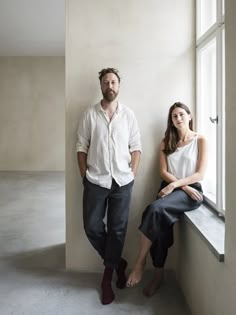 a man and woman standing next to each other near a window in an empty room