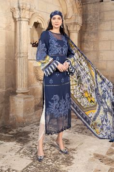 a woman standing in front of a stone wall wearing a blue dress with paisley print on it