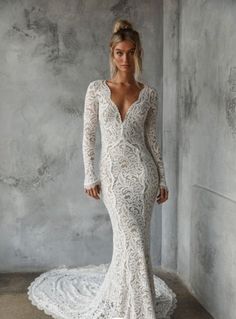 a woman in a long sleeved wedding dress standing against a wall with her hands on her hips