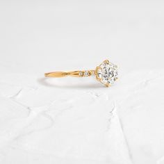 an engagement ring with a diamond in the center on a white surface, it is gold and has a twisted band