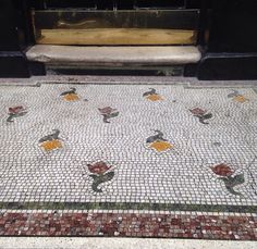 a bench sitting on the side of a building next to a tiled floor with flowers