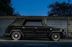 an old black car parked in front of a garage door at night with the lights on