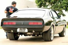 a man standing next to a car with the hood down and it's tail lights on