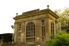 an old stone building with arched windows on the top and bottom floor, surrounded by greenery