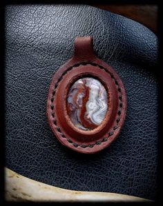 "Handmade leather bound Crazy Lace Agate pendant. 2 3/4 inches long. Can be put on a dark brown or black leather cord or a copper or brass chain. Please choose from the options. Default choice is a 24\" copper chain." Handmade Rust Leather Jewelry, Artisan Jewelry With Leather Strap For Gift, Brown Leather Pendant Necklace, Everyday Use Brown Pendant Jewelry, Brown Pendant Jewelry For Everyday Use, Brown Waxed Finish Jewelry As Gift, Brown Jewelry With Waxed Finish As Gift, Artisan Hand Tooled Jewelry, Unique Jewelry With Leather Strap For Gift