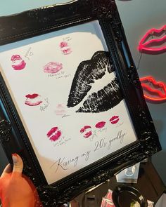 a person holding up a framed poster with lipstick on it