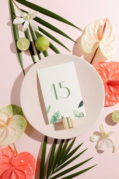 an arrangement of flowers and greenery with a table number on the plate next to it