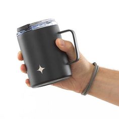 a hand holding a black cup with a silver star on the side and a white background