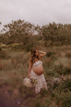 a pregnant woman standing in a field with her hands on her head and holding a basket