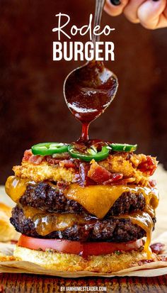 A rodeo burger piled high with tomato, two beef patties, melted cheddar cheese, crispy bacon, jalapeños, and onion rings.  A spoon is drizzling on bbq sauce. Bbq Sauce For Burgers, Elevated Burger Recipes, Rodeo Burger Recipe, Fancy Burgers Ideas, Western Burgers Recipes, Smash Burger Ideas, Best Burger Recipes, Creative Burger Ideas, Beef Burgers Recipes