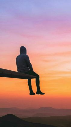 a man sitting on top of a wooden bench at the top of a hill during sunset