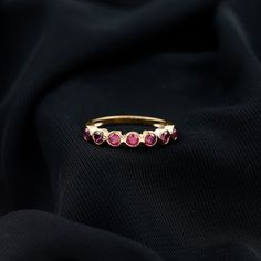 a gold ring with five pink stones on black fabric background, closeup view from above