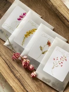 four cards with flowers on them sitting on top of a wooden table next to each other