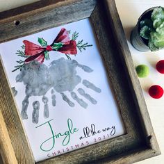 a handprint christmas ornament is displayed in a wooden frame next to other holiday decorations