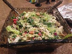 a salad in a glass dish on a counter next to some tinfoil wrappers