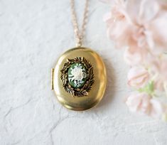 This is a large gold locket necklace. It is made from a vintage oval shaped brass locket and adorned with a beautifully detailed brass leaf wreath and a vintage floral resin cameo. The locket is quit large and holds space for two special photos. Measurements & Details - locket size: 45mmx38mm, gold tone brass - chain: vintage brass chain PERSONALISATION We can personalize this locket by adding 1 or 2 photos for you. You can also choose to add photo (s) on your own. Please choose from drop-do Oval Cameo Keepsake Jewelry, Oval Vintage Charm Locket Necklace For Wedding, Oval Cameo Necklace Keepsake, Oval Cameo Necklace For Keepsake, Wedding Vintage Charm Oval Locket Necklace, Wedding Oval Pendant Locket Necklace In Antique Gold, Antique Gold Oval Pendant Necklace For Wedding, Vintage Cameo Locket Necklace For Wedding, Gold Cameo Locket Necklace For Wedding