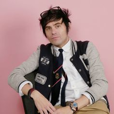 a man sitting on top of a chair wearing a vest and tie with his hands in his pockets