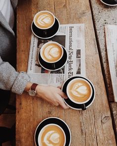 two people sitting at a table with cups of coffee in front of them and newspapers on the table