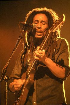 a man with dreadlocks on his head playing guitar and singing into a microphone