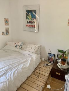 a bed with white sheets and pillows on top of a wooden floor next to a table