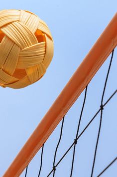 a yellow ball that is in the air near a net on a beach volleyball court