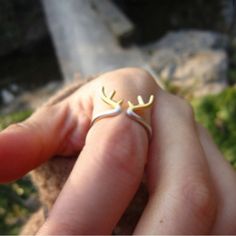 a hand holding a tiny ring with two antlers on it's middle finger