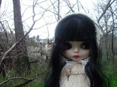 a doll with long black hair standing in the woods