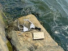 a book and headphones sitting on top of a rock next to the ocean water