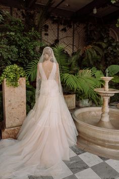 the back of a bride's dress in front of a fountain with greenery