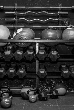 black and white photograph of kettles and dumbbells on a rack in a gym