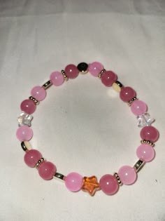 a pink beaded bracelet with an orange star charm on it's end and a gold plated clasp