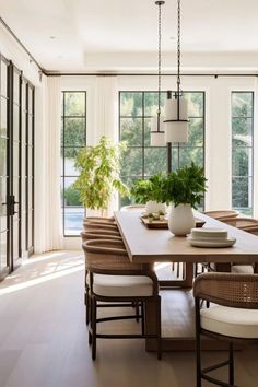 a dining room table with chairs and a potted plant in the center is surrounded by large windows