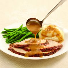 a white plate topped with meat covered in gravy next to green beans and mashed potatoes