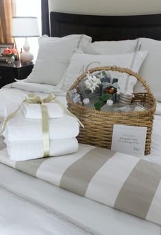 a bed with white sheets and pillows on top of it next to a basket filled with gifts