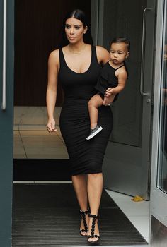 a woman in a black dress holding a small child while walking out of a building