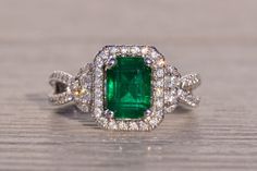 an emerald and diamond ring sitting on top of a wooden table