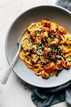 a bowl filled with pasta and meat on top of a blue table cloth next to a fork