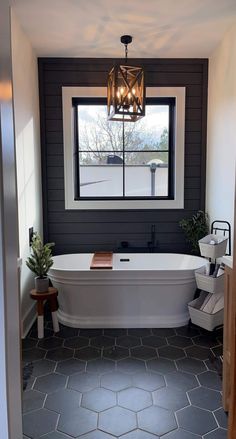 a white bath tub sitting under a window next to a wooden table and potted plant