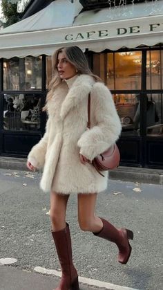 a woman is walking down the street wearing boots and a coat with fur on it