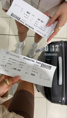 two people standing next to each other in front of a luggage bag and holding tickets