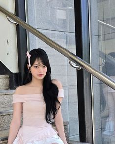 a young woman sitting on the steps in front of a glass door wearing a pink top and white skirt