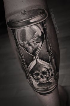 a man's leg with an hourglass tattoo on it and a skull in the sand