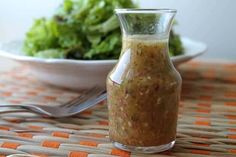 there is a small glass bottle on the table next to a bowl of lettuce