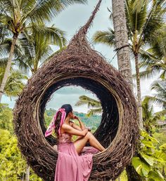 a woman in a pink dress standing next to a bird nest with palm trees behind her